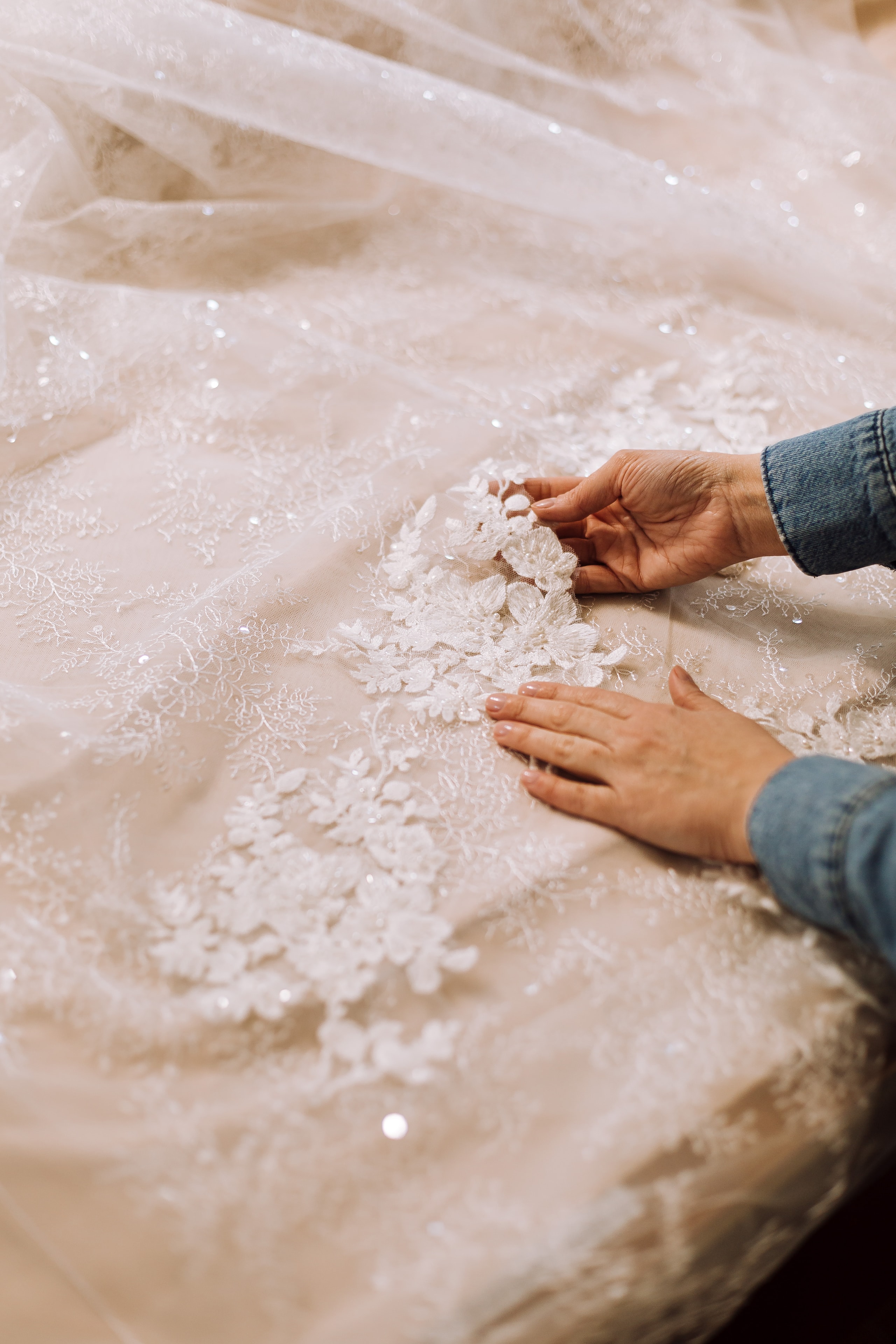Artisan hands smoothing intricate lace appliqué on a bridal gown